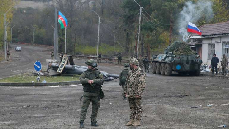 An Azerbaijani service member and a Russian peacekeeper stand guard at a checkpoint on the outskirts of Shusha
